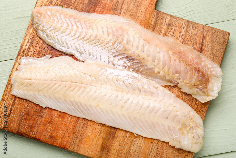 Board with raw codfish fillet on green wooden background