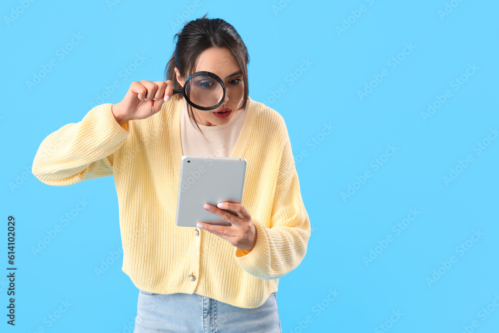 Young woman with magnifier and tablet computer on blue background