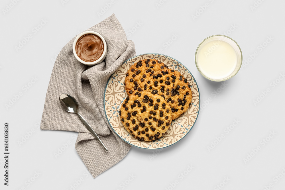 Plate with cookies, glass of milk and towel on light background