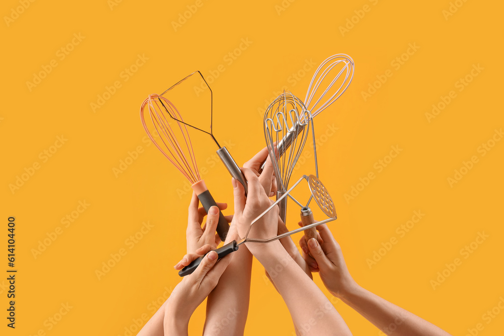 Female hands holding different whisks and mashers on yellow background