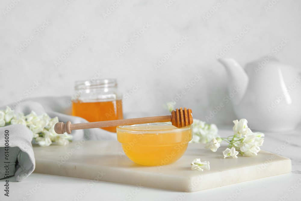 Bowl of honey with flowers of acacia on light background, closeup