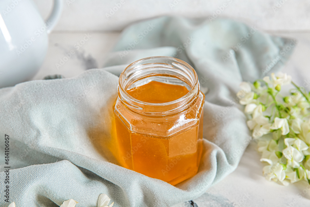 Jar of honey with flowers of acacia on light background, closeup