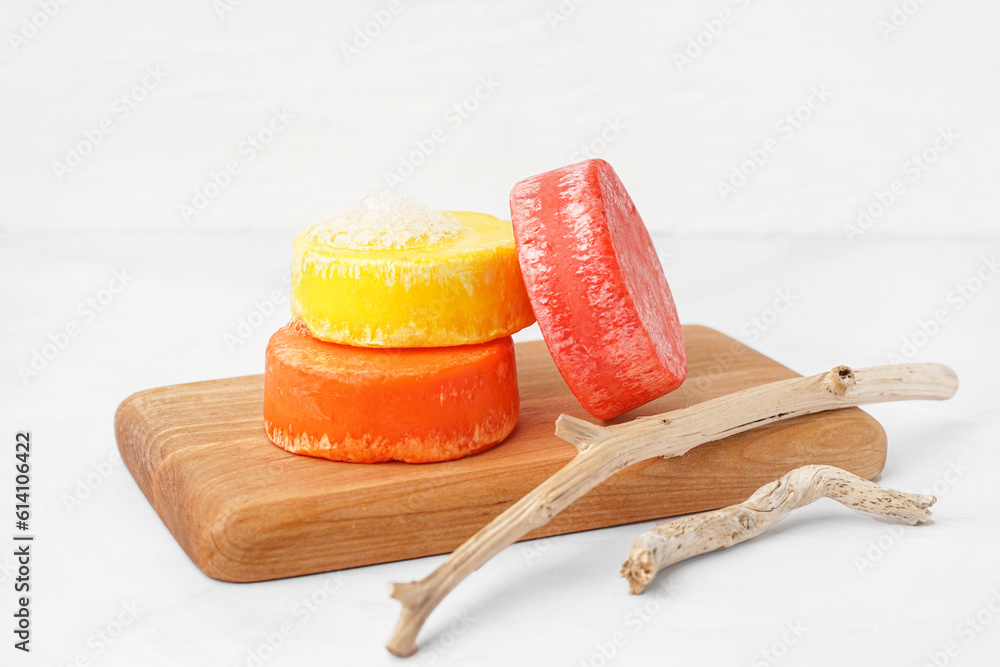 Board with different handmade solid shampoo and branches on light background, closeup