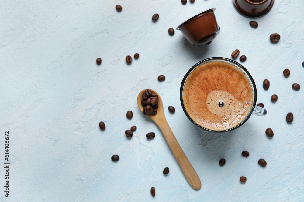 Cup of delicious coffee, wooden spoon, beans and capsules on blue table