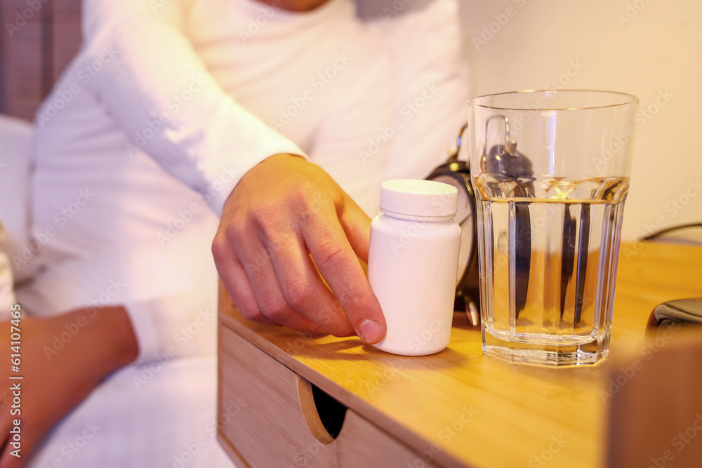 Young man taking pill bottle in bedroom at night, closeup