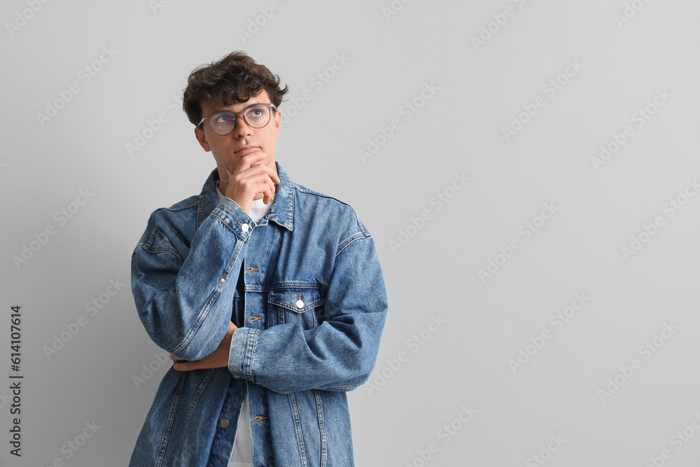 Thoughtful young man in stylish eyeglasses on light background