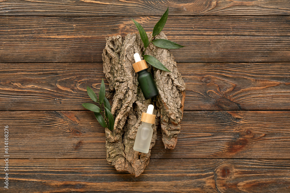 Bottles of essential oil, tree bark and plant leaves on wooden background