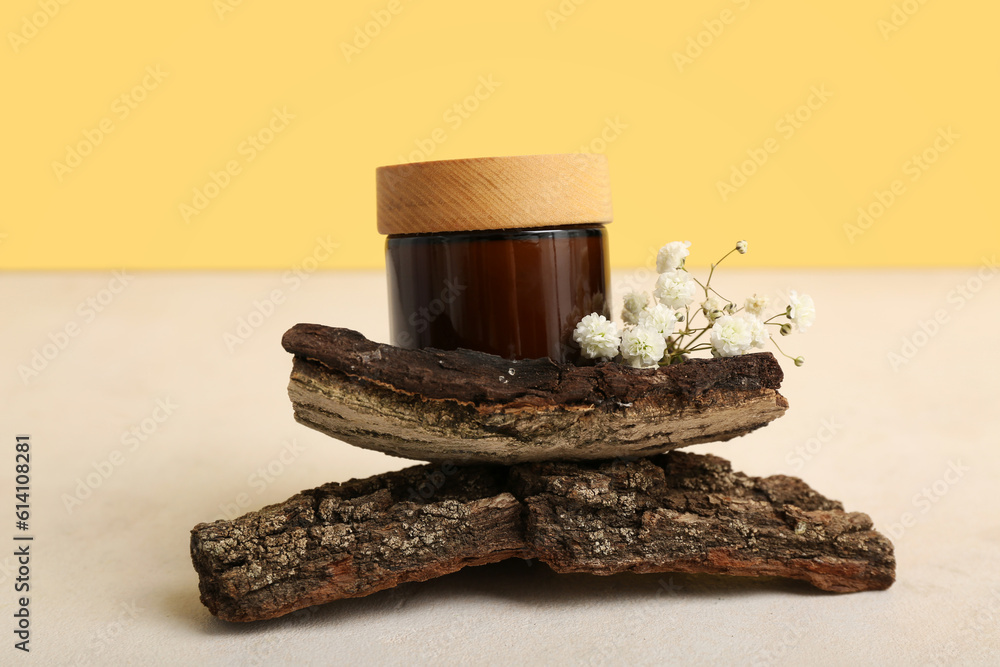 Jar of cosmetic product, tree bark and gypsophila flowers on light table