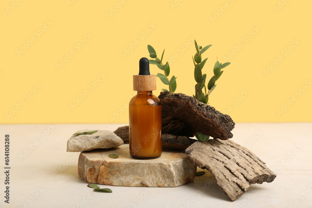 Composition with bottle of essential oil, stones, tree bark and eucalyptus branches on table against