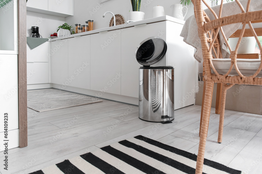 Opened metallic trash bin near table in interior of modern kitchen