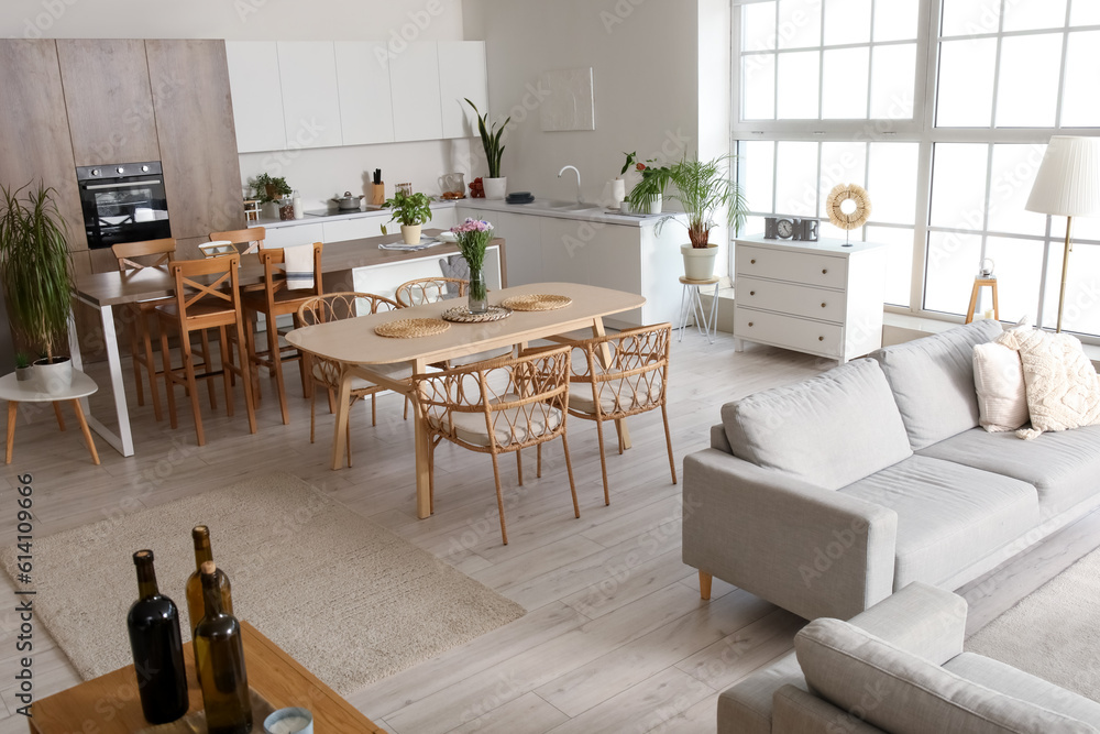 Interior of light open plan kitchen with dining table, island and grey sofa