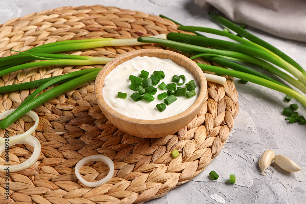 Bowl of tasty sour cream with sliced scallion and onion on grey background