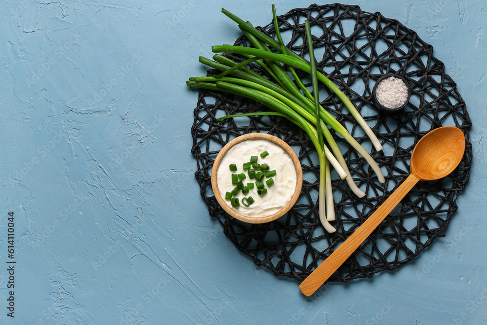 Bowl of tasty sour cream with green onion on blue background