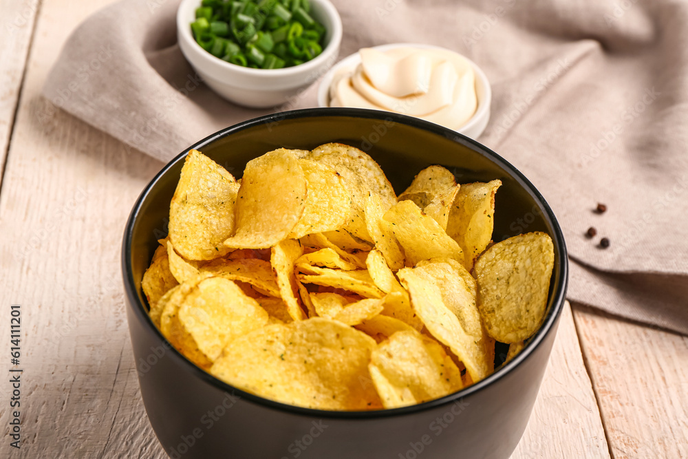 Bowls of tasty sour cream with sliced green onion and potato chips on white wooden background