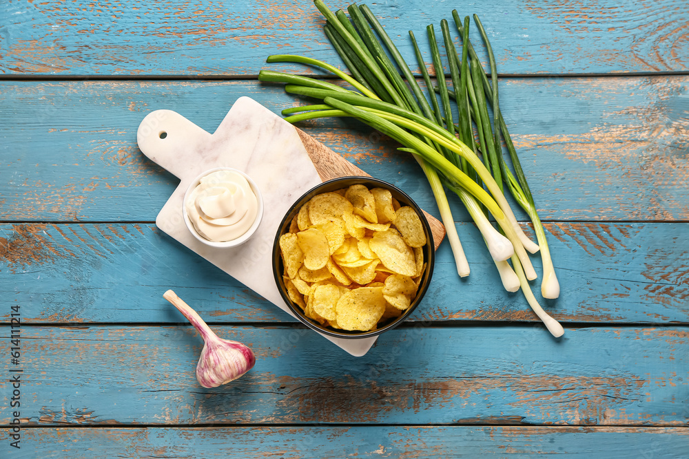 Bowl of tasty sour cream with green onion and potato chips on blue wooden background