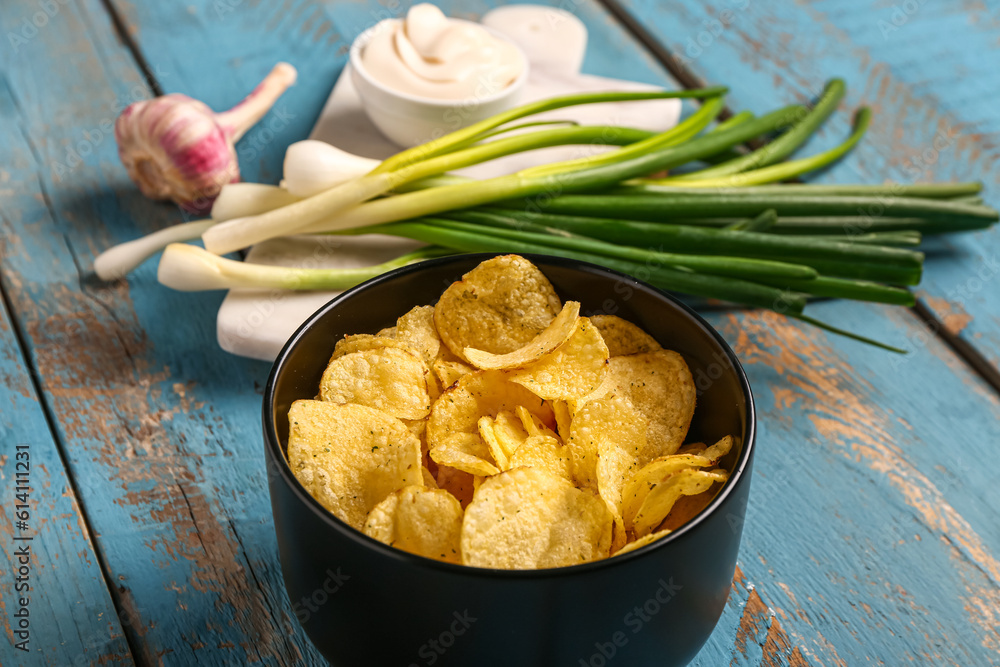 Bowl of tasty sour cream with green onion and potato chips on blue wooden background