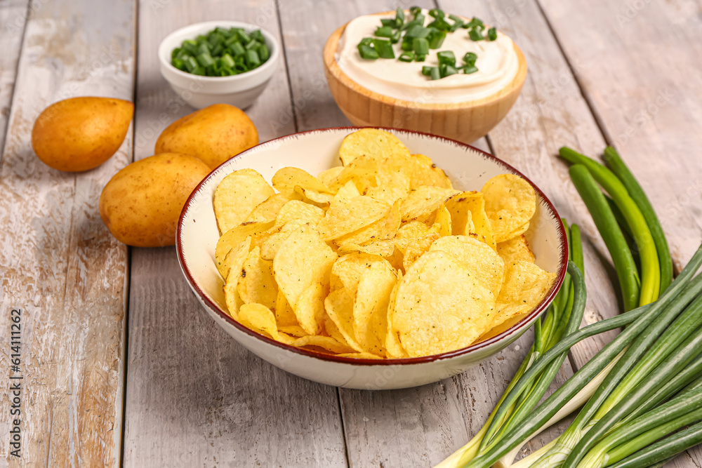 Bowls of tasty sour cream with sliced green onion and potato chips on grey wooden background