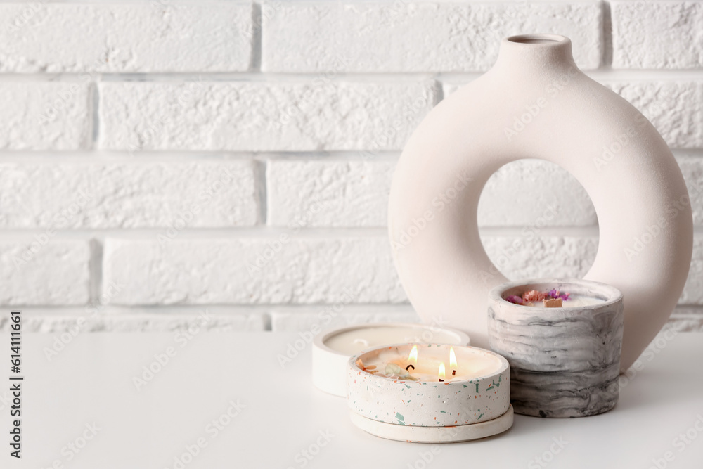 Holders with burning candles and decor on table near light brick wall in room