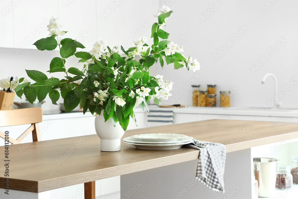 Vase with blooming jasmine flowers on wooden table in modern kitchen