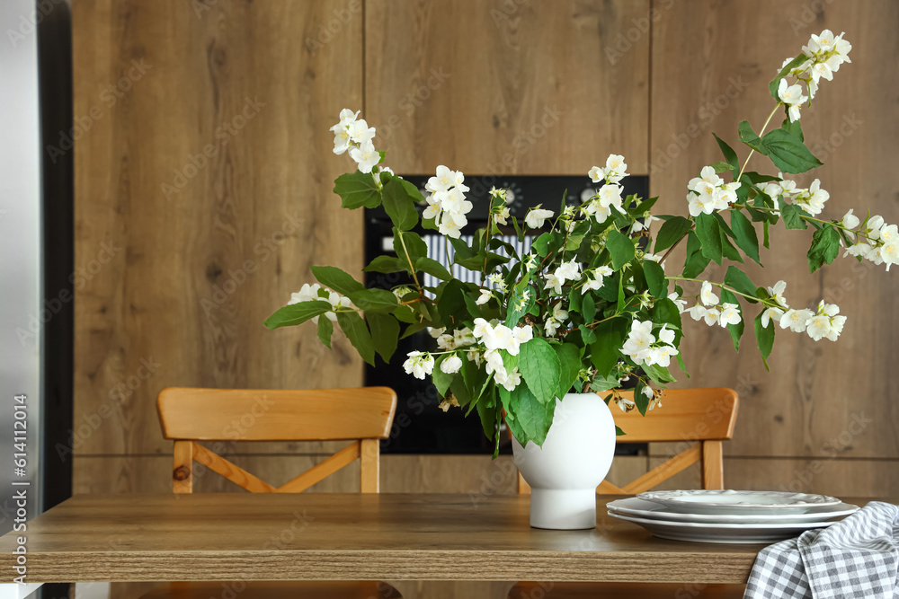 Vase with blooming jasmine flowers on wooden table in modern kitchen