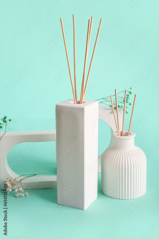 Bottles of reed diffuser and flowers on turquoise background