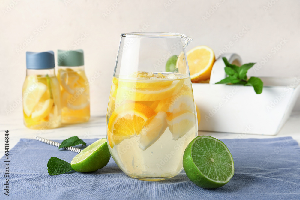 Jug of infused water with citrus fruits on light background