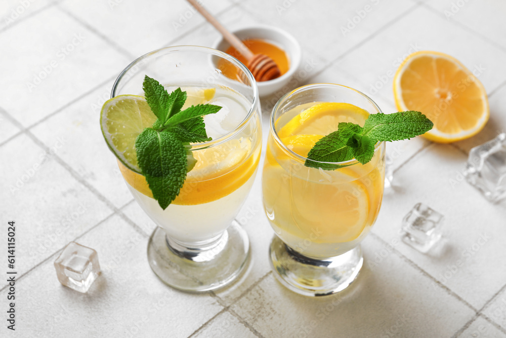 Glasses of infused water with lemon on white tile background