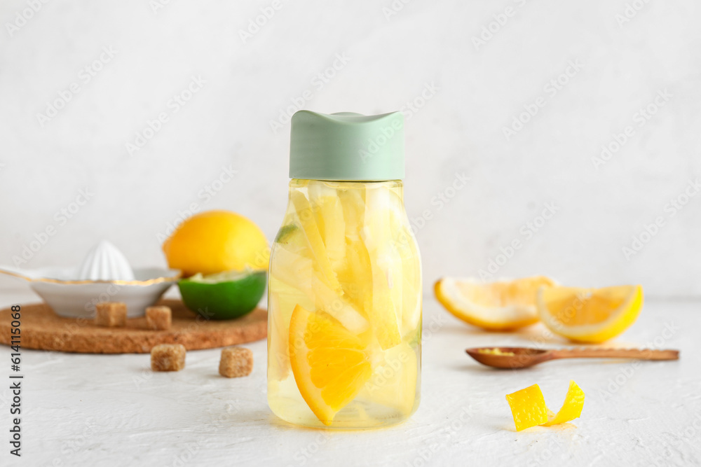 Bottle of infused water with lemon on light background