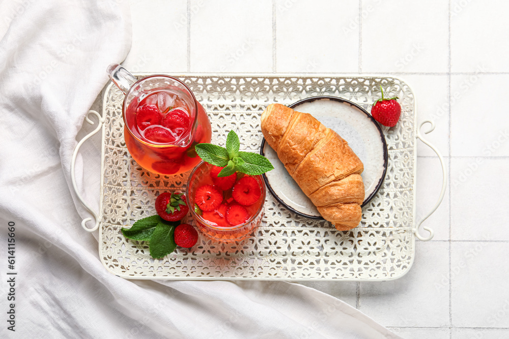 Tasty croissant, jug and glass of infused water with strawberry on white tile background