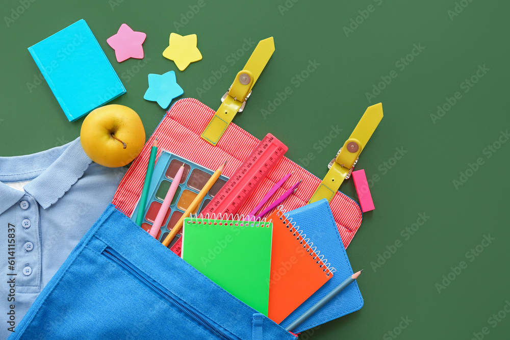 Backpack with shirt, apple and different stationery on green background