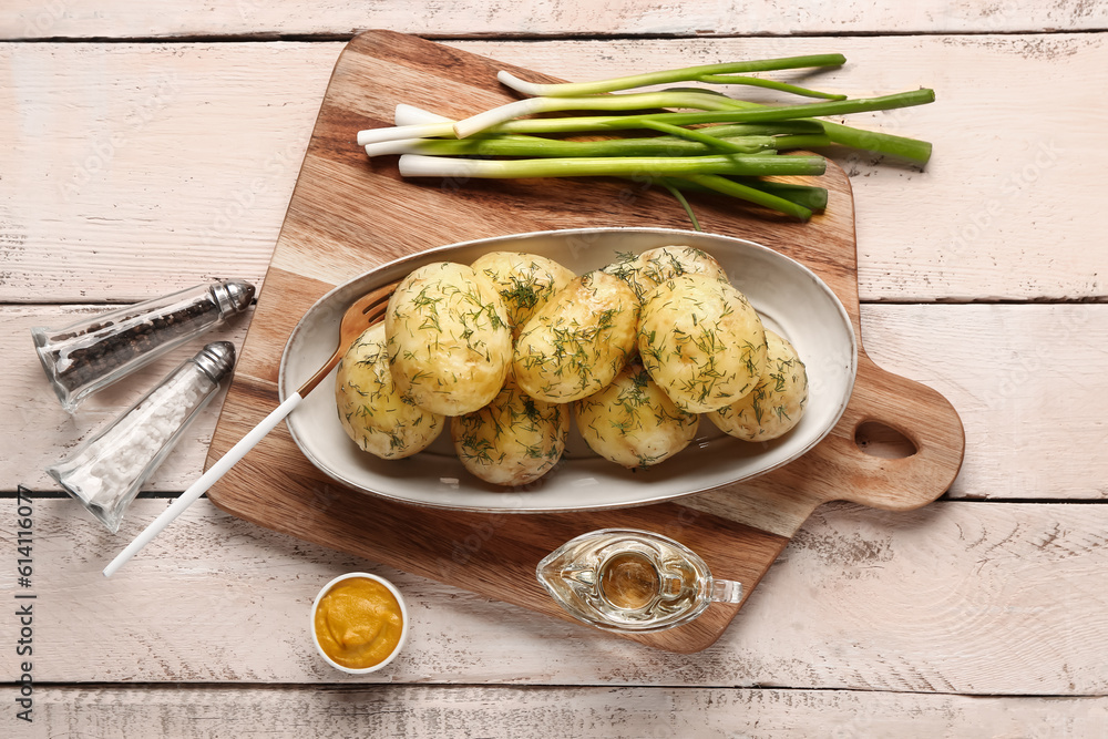 Plate of boiled baby potatoes with dill and green onion on white wooden background