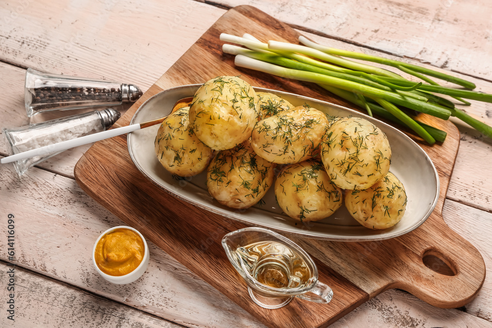 Plate of boiled baby potatoes with dill and green onion on white wooden background