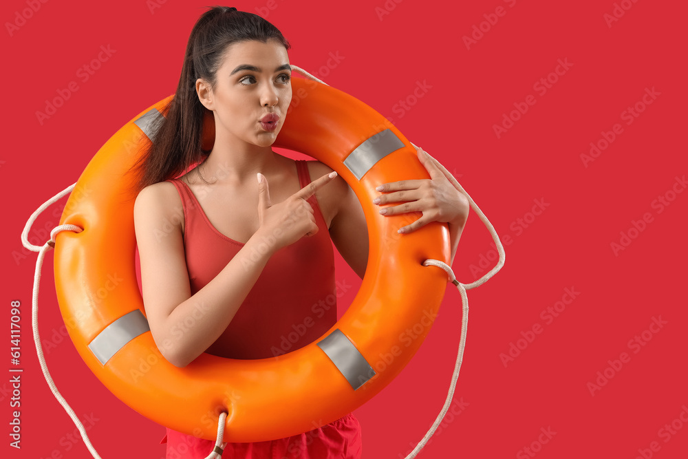 Female lifeguard with ring buoy pointing at something on red background