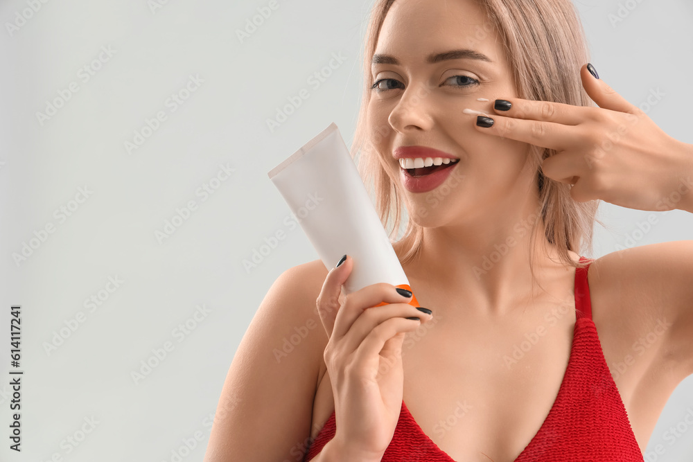 Young woman applying sunscreen cream on her face against light background, closeup