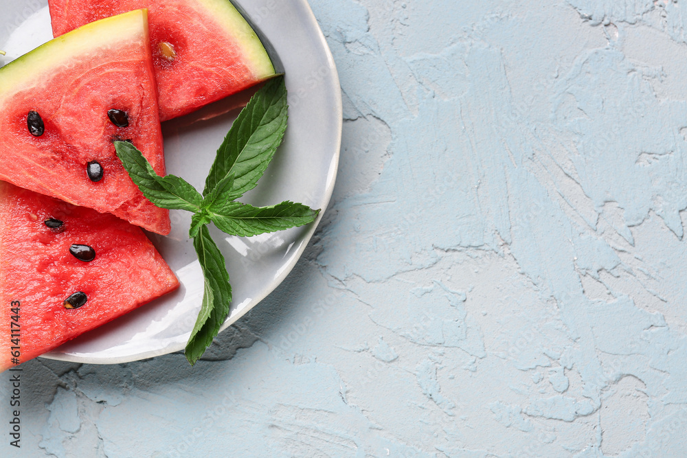 Plate with pieces of fresh watermelon and mint on blue background