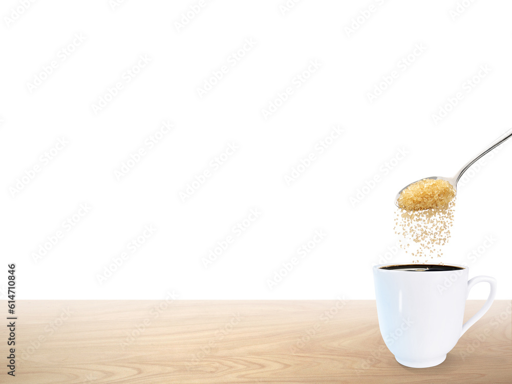 A spoonful of granulated sugar is poured into a white coffee mug placed on a wooden floor.