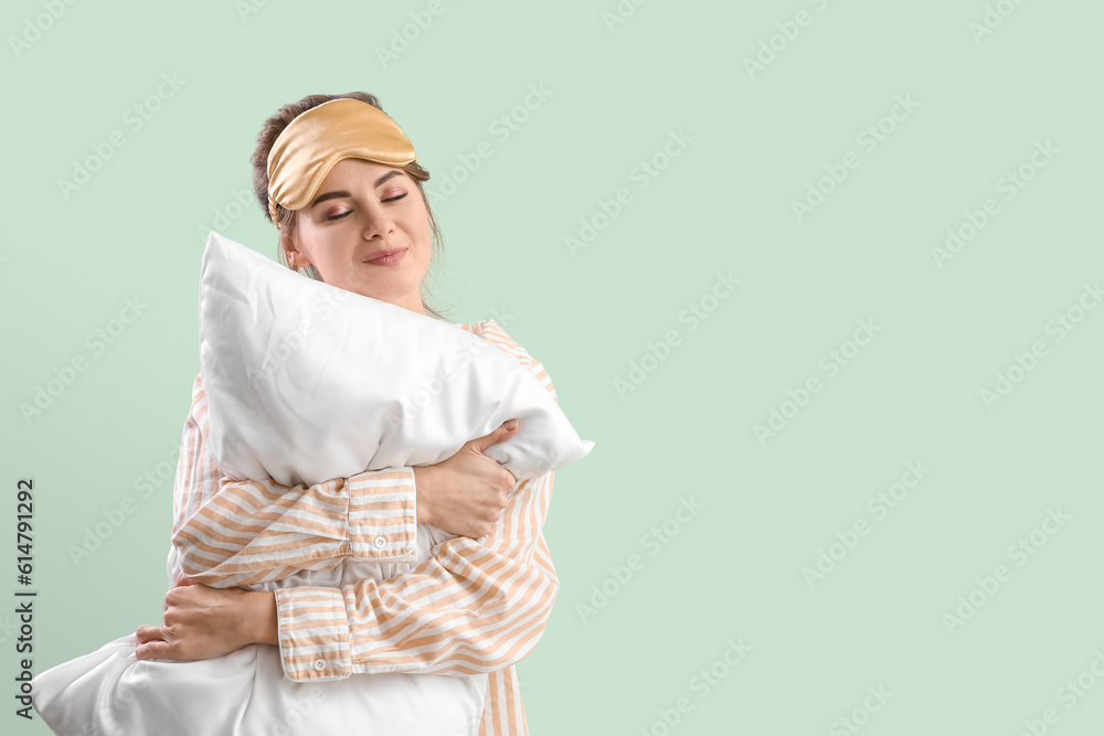 Beautiful woman with sleeping mask and pillow on green background