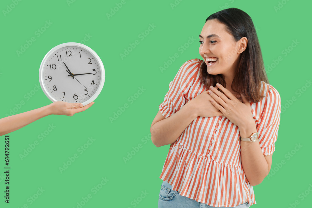 Happy young woman with wristwatch and wall clock on green background