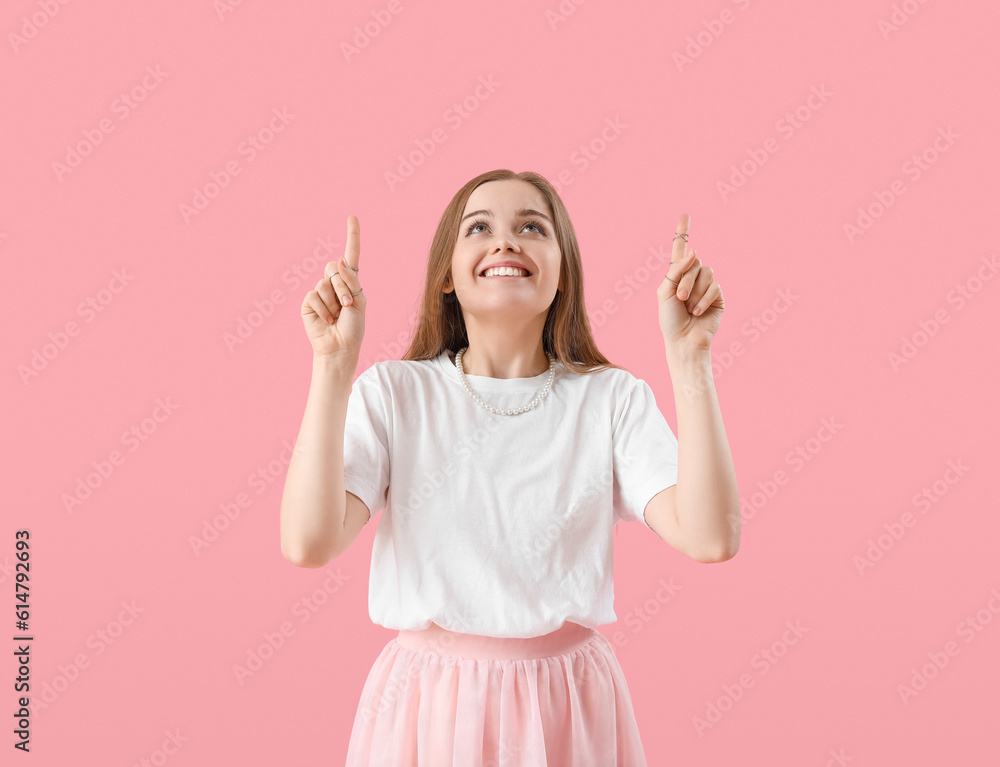 Young woman in t-shirt pointing at something on pink background