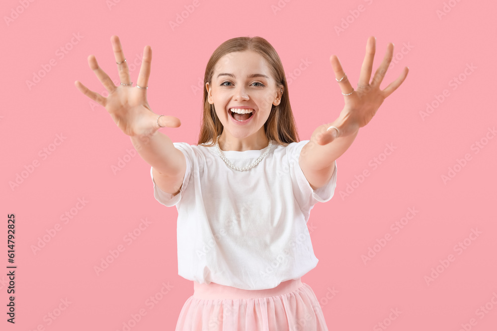 Happy young woman in t-shirt showing hands on pink background