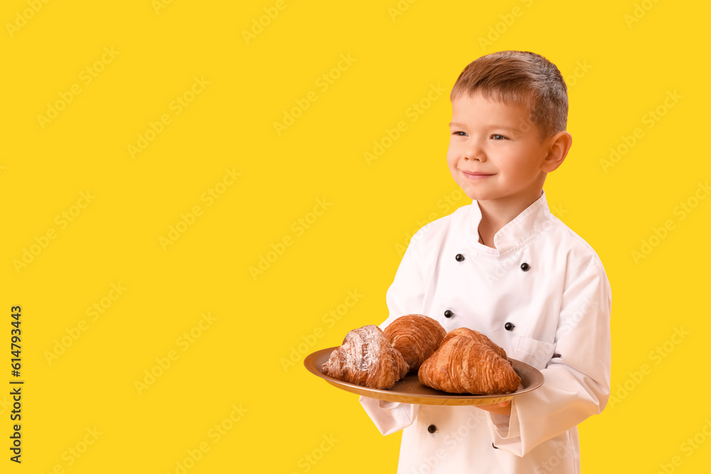 Cute little chef with tray of croissants on yellow background