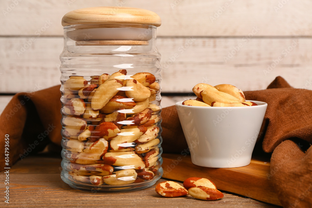 Glass jar and bowl of tasty Brazil nuts on wooden table