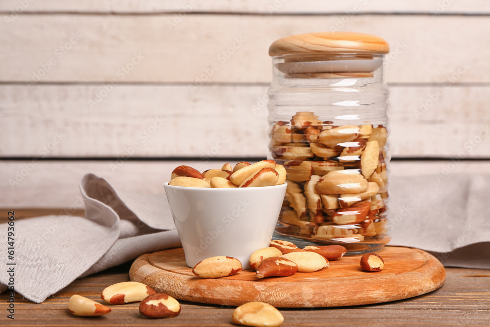 Glass jar and bowl of tasty Brazil nuts on wooden table