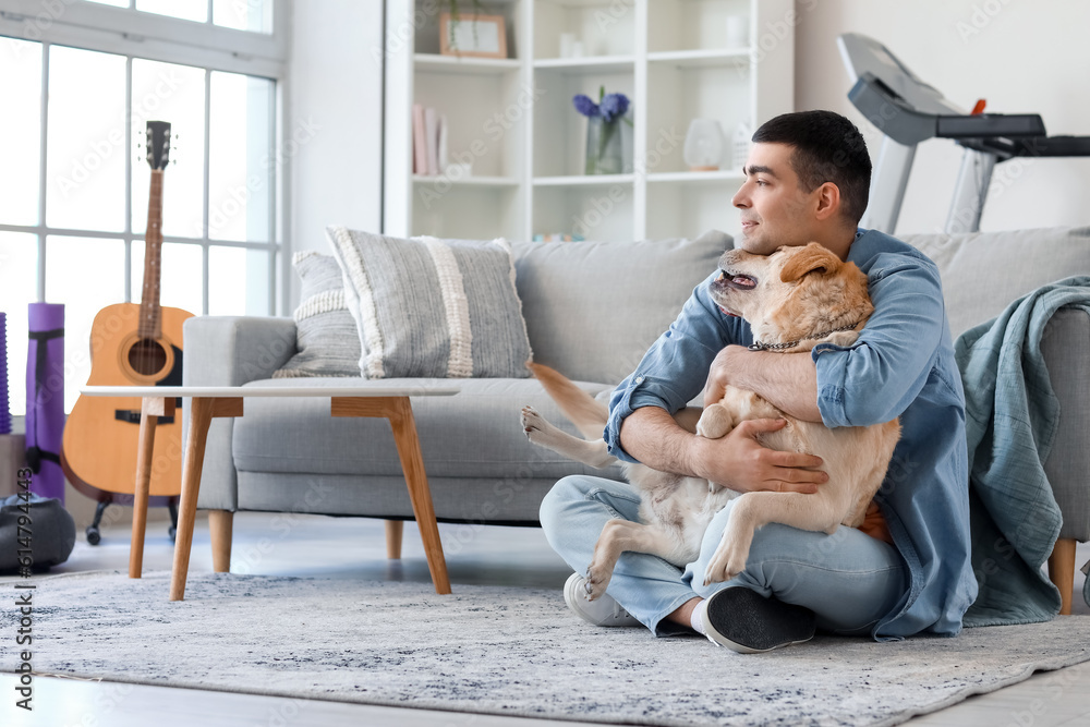 Young man with cute Labrador dog sitting on floor at home