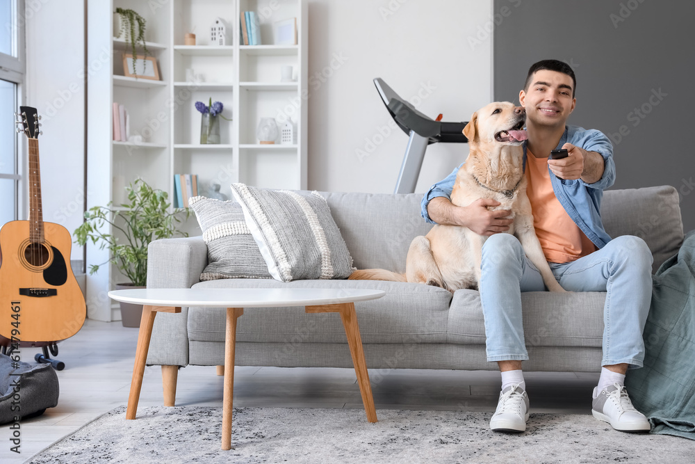 Young man with cute Labrador dog watching TV on sofa at home