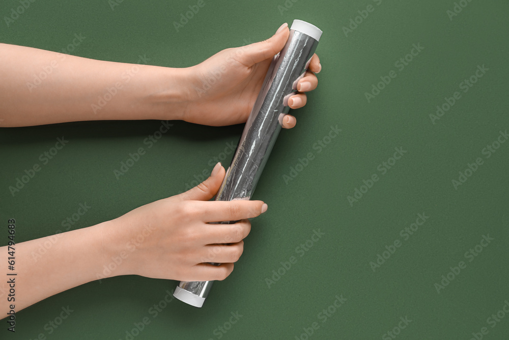 Female hands with roll of aluminium foil on green background