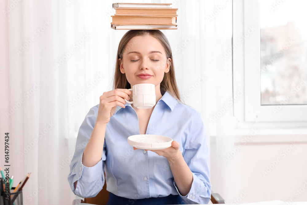 Young businesswoman with books drinking coffee in office. Balance concept