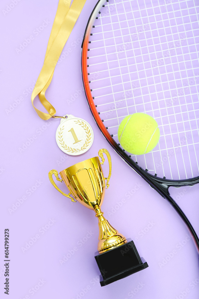 Gold cup with first place medal, tennis racket and ball on lilac background