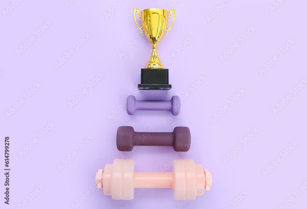 Gold cup with dumbbells on lilac background