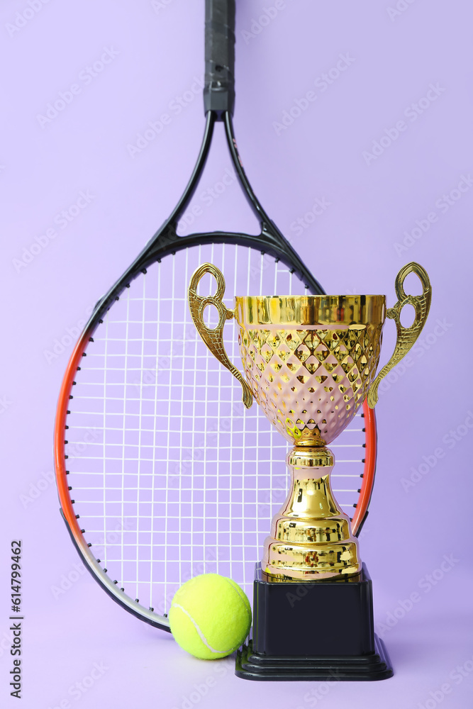 Gold cup with tennis racket and ball on lilac background